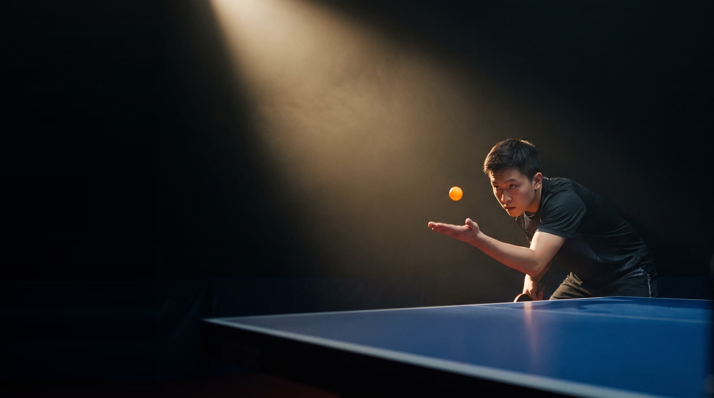 A player frozen at the moment of a serve toss in a dark tournament hall
